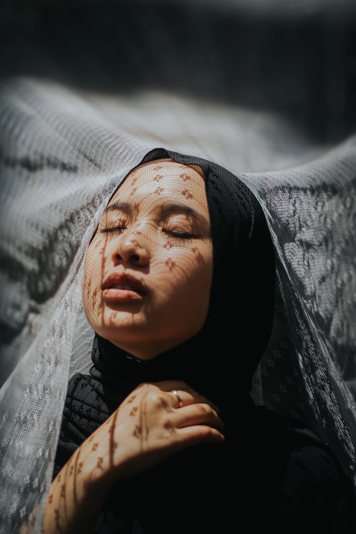 services-04 Emotive portrait of a woman with lace veil patterns in soft light.